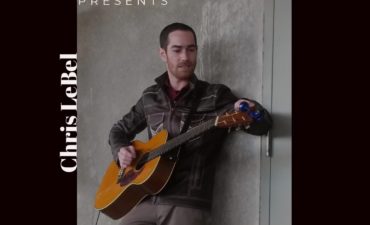 photo of Chris LeBell with guitar against a wall