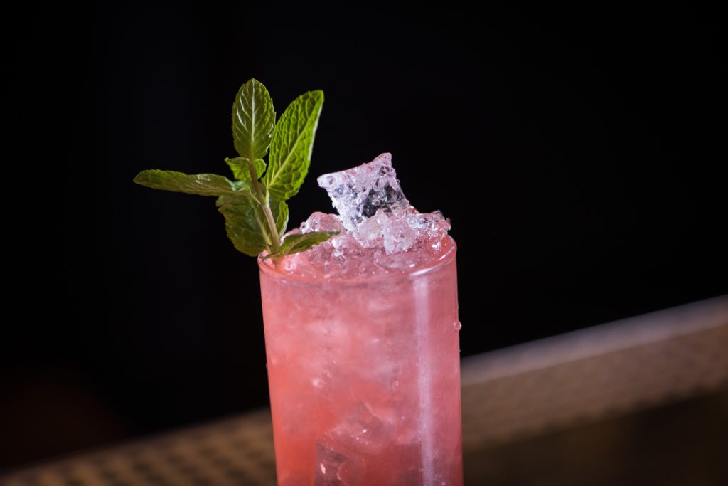 a decorative picture of a pink drink with ice cubes and mint garnish