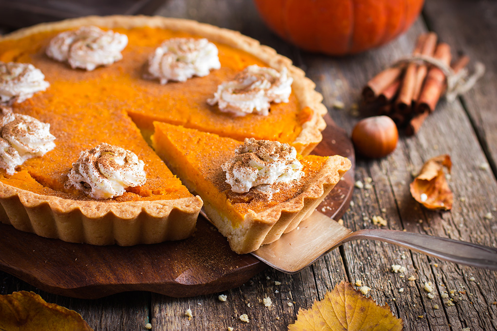 picture of pumpkin pie with slice partly removed on a wooden table