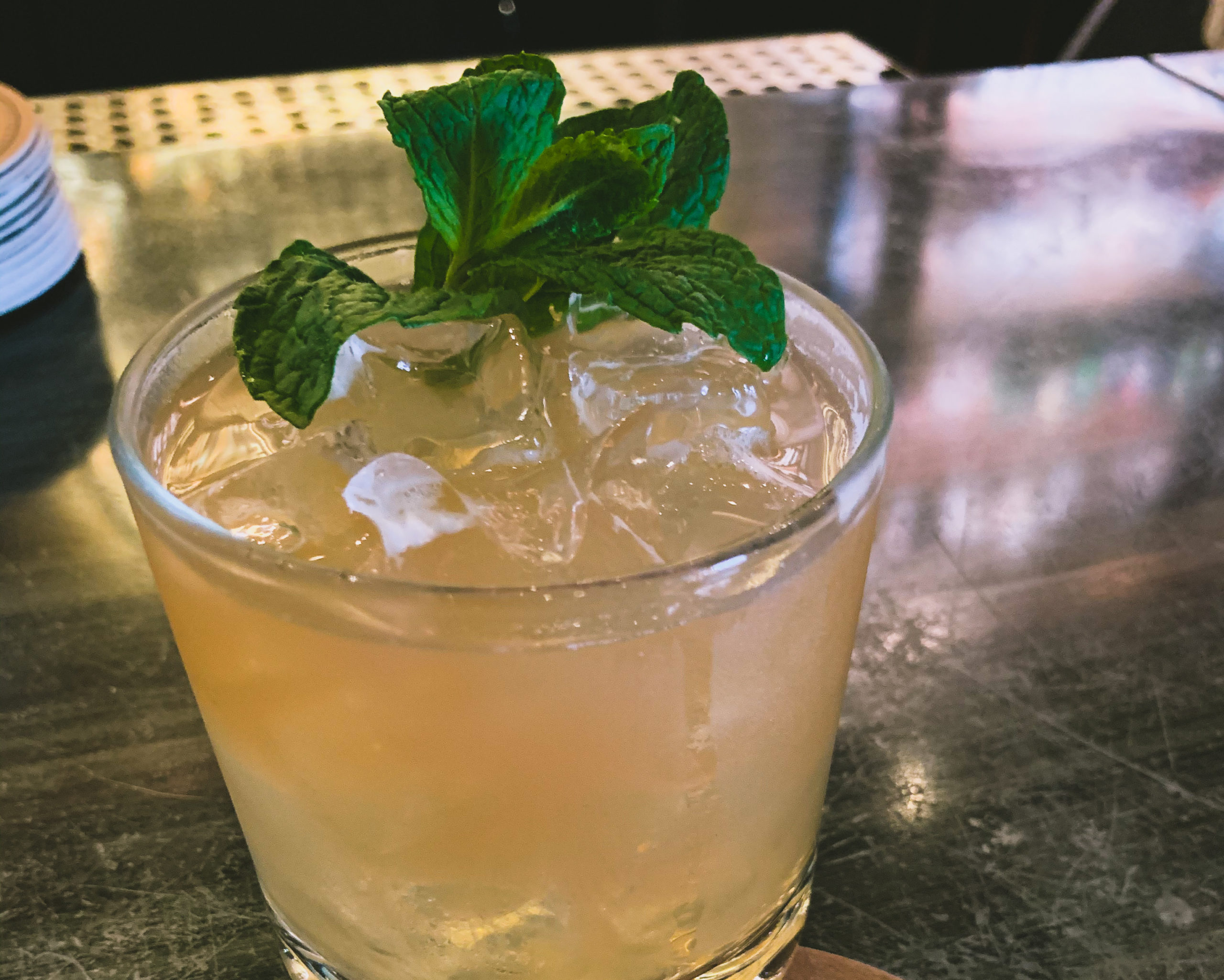 a photo of the suffering bastard cocktail in an old fashioned glass with sprig of mint on the bar