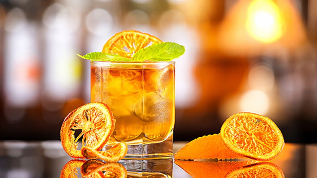 Classic Mai Tai cocktail in a rocks glass with dried orange garnish and mint, set against a softly lit bar background.