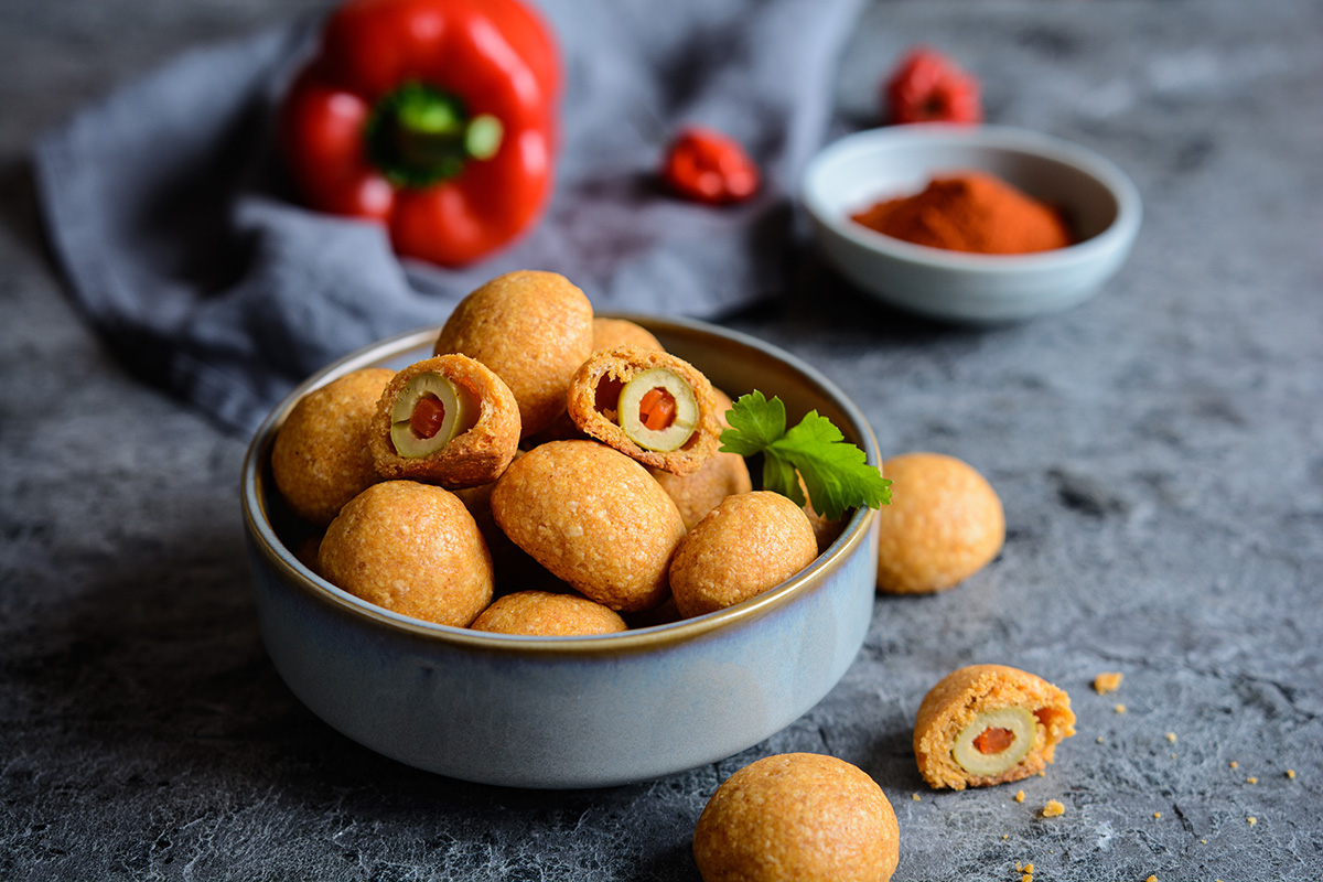 baked green olives coated in cheese and paprika dough in gray bowl