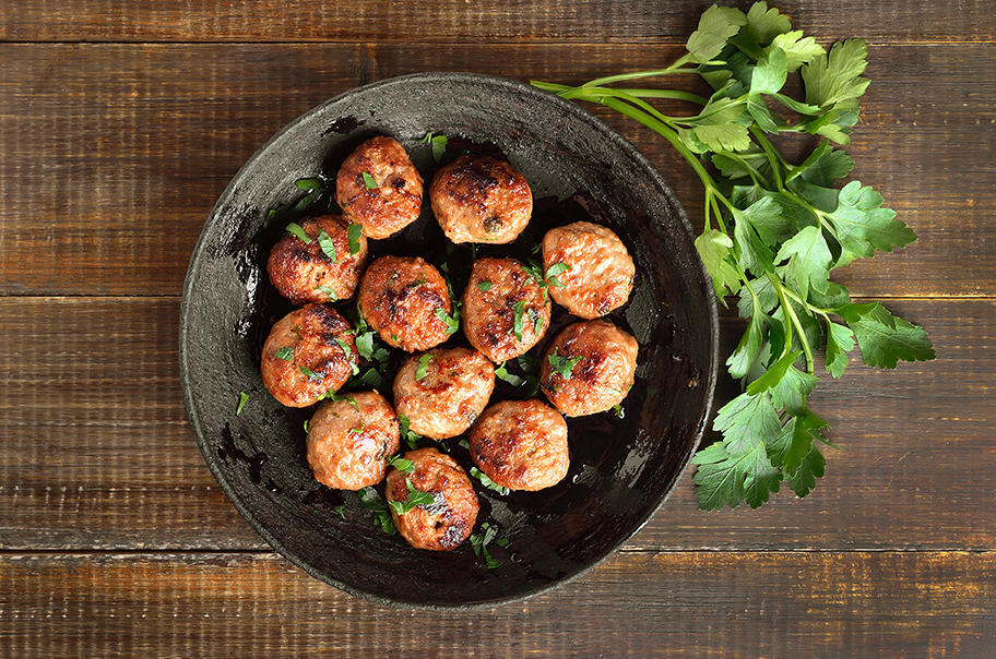 MEATBALLS IN A GRAY BOWL ON WOOD TABLE WITH PARSLEY