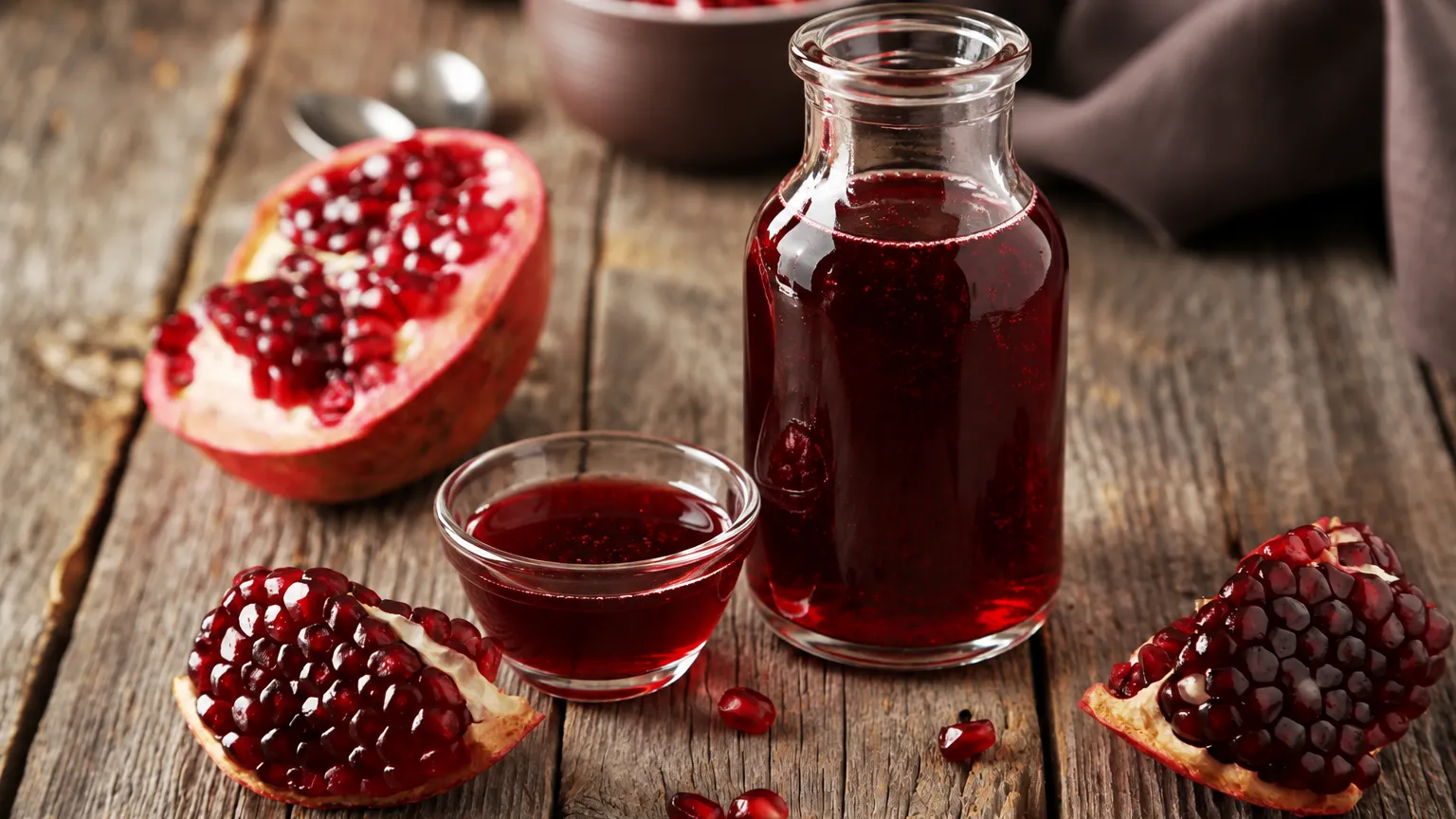 grenadine syrup in a bottle on a wooden table surrounded by pomegranates.