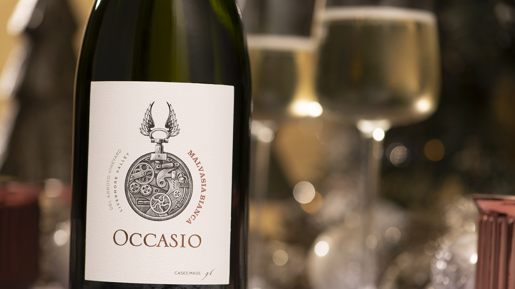 close up of Occasio Malvasia Bianca sparkling wine with filled glasses blurred in background.