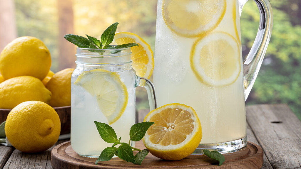 pitcher of lemonade and a mug of lemonade with lemons on the side garnished with mint