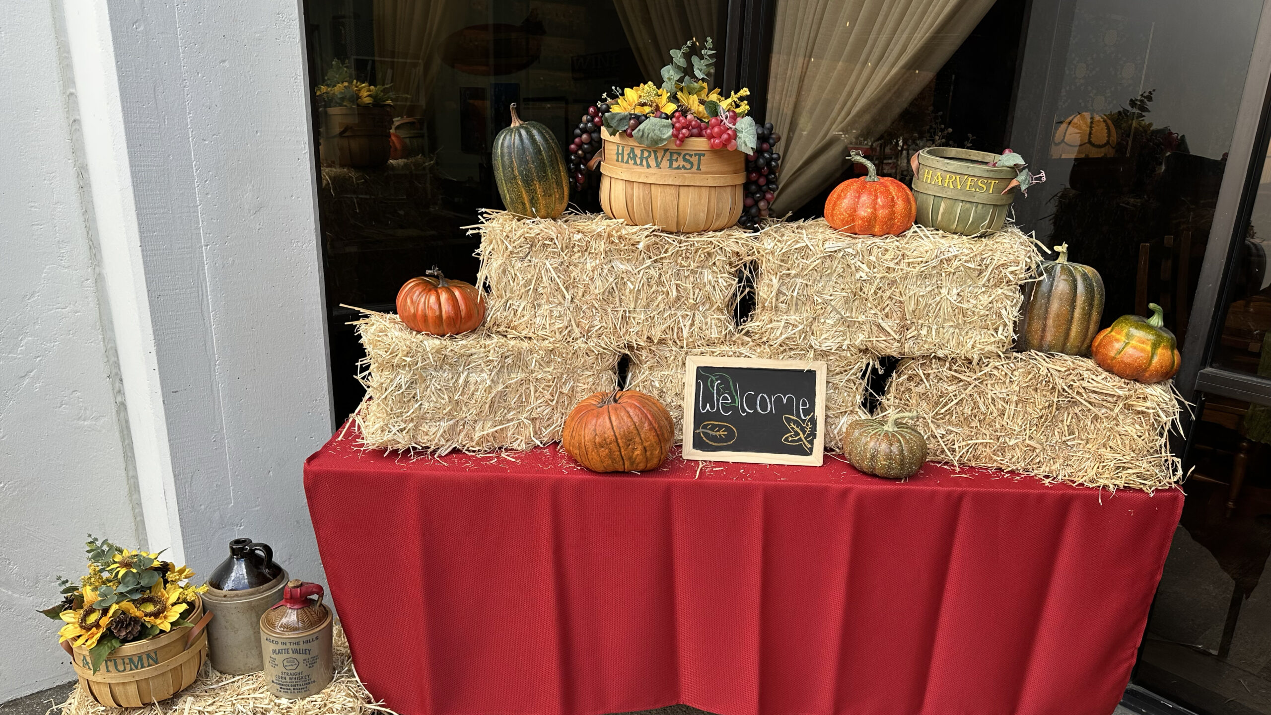 table with orange table cloth stacked high with hay bales pumpkins and fall baskets